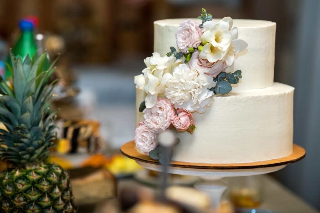 Tall sweet wedding cake decorated with live pink and white flowers on a table.