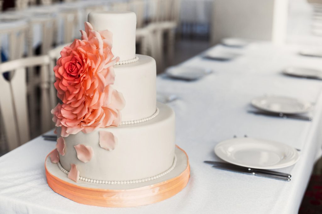 Three tiered luxury white wedding cake with orange flower petals from mastic on table